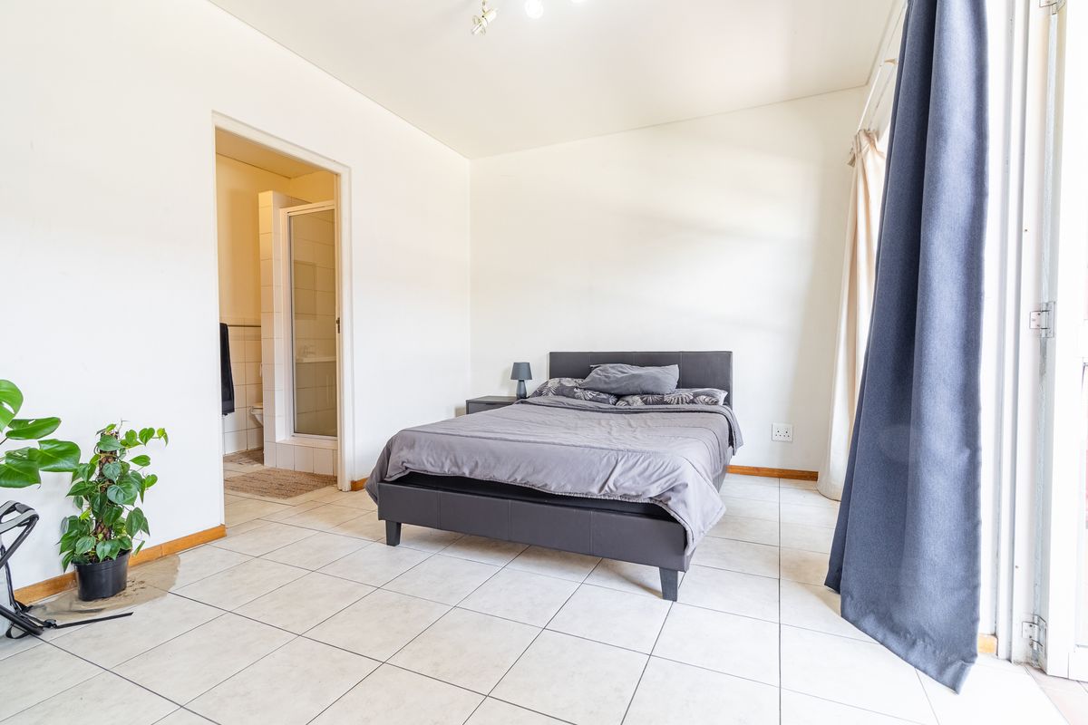 A bedroom featuring tiled flooring, an en-suite bathroom with a shower, and a sliding door providing access to the exterior.