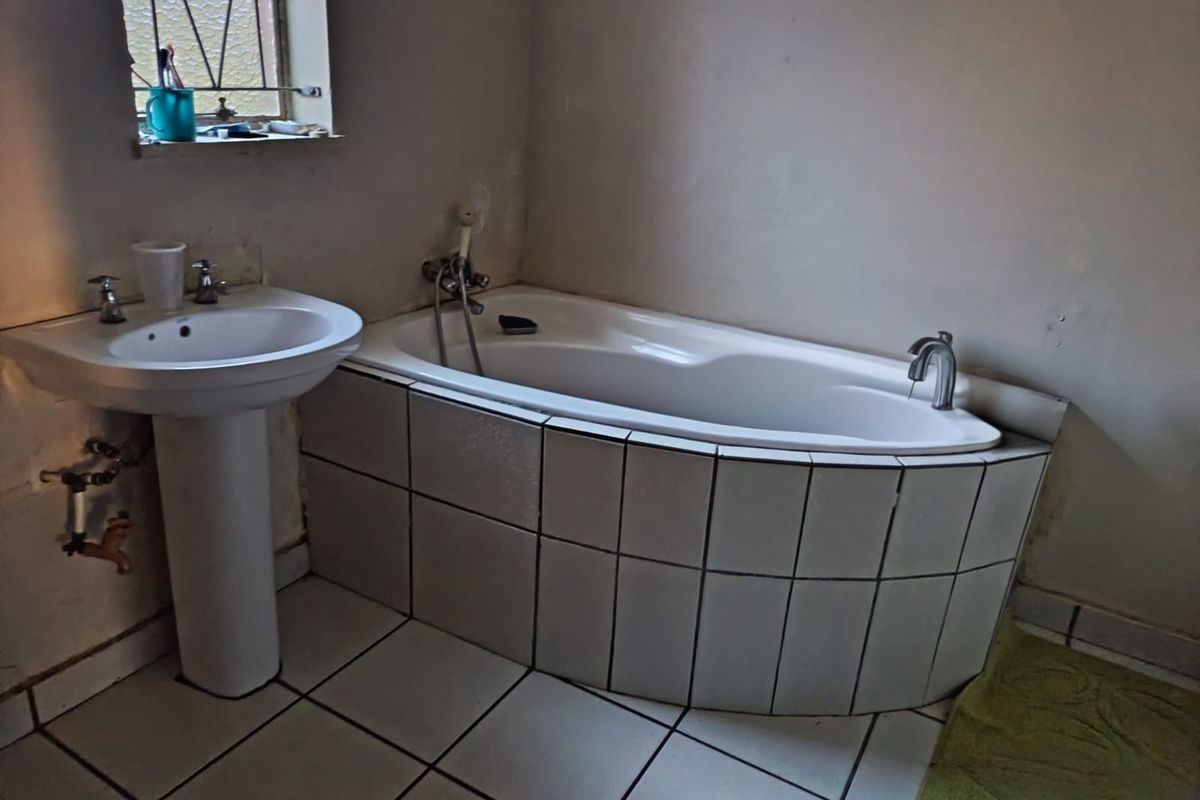 A functional bathroom featuring a pedestal basin and a tiled bathtub, requiring cosmetic updates to the wall finishes and general maintenance.