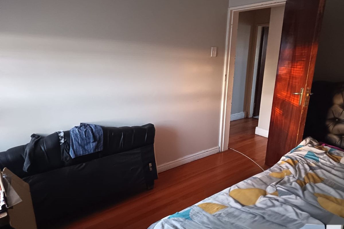 A bedroom featuring hardwood flooring and a timber door, providing access to an adjacent hallway.