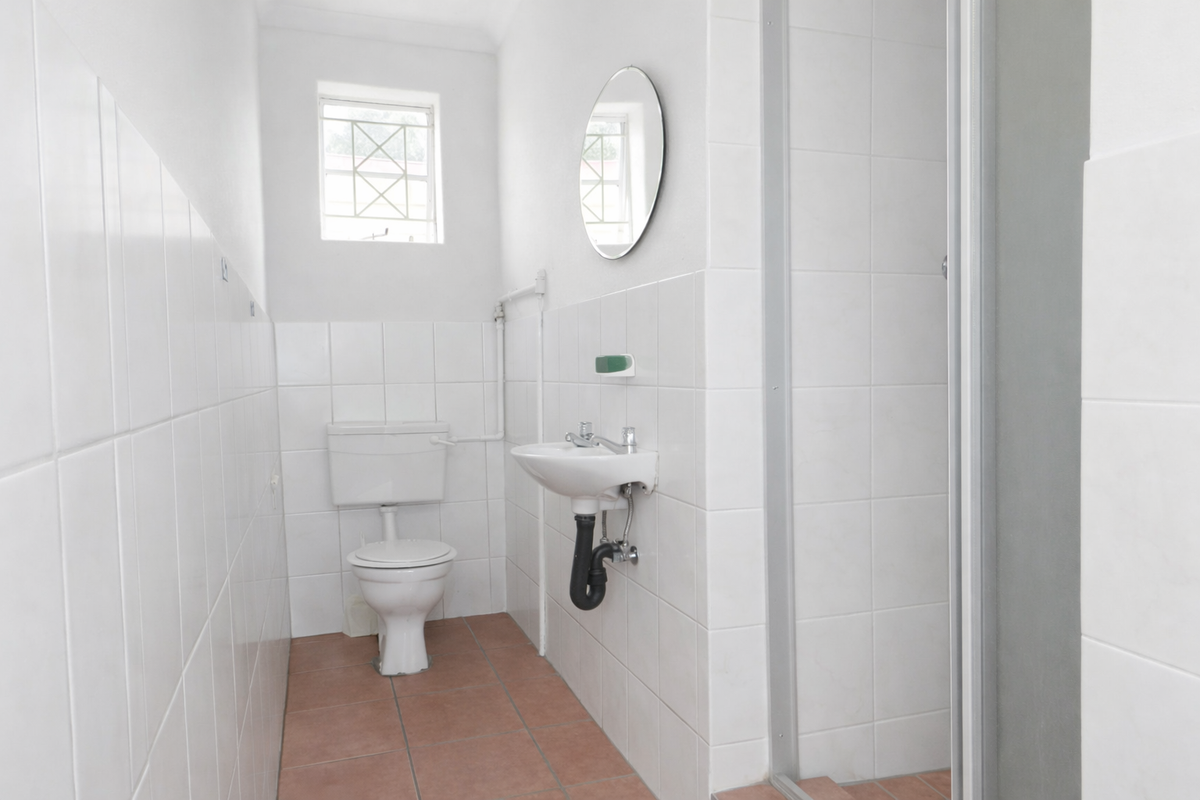 A functional bathroom featuring a white toilet, wall-mounted basin, and a shower enclosure with tiled walls and flooring.
