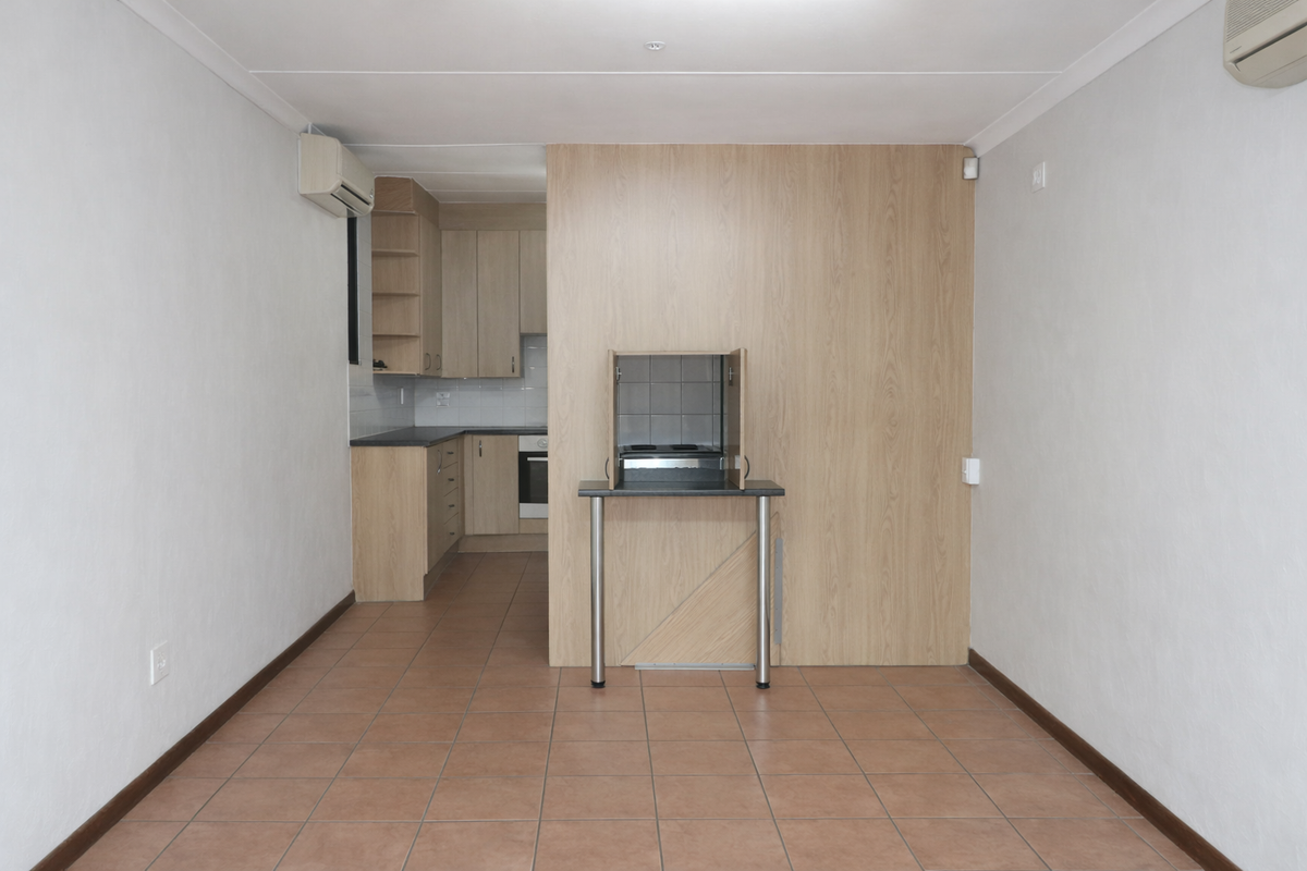 An open-plan living area featuring a compact kitchen with light wood cabinetry, tiled flooring, and a wall-mounted air conditioning unit.