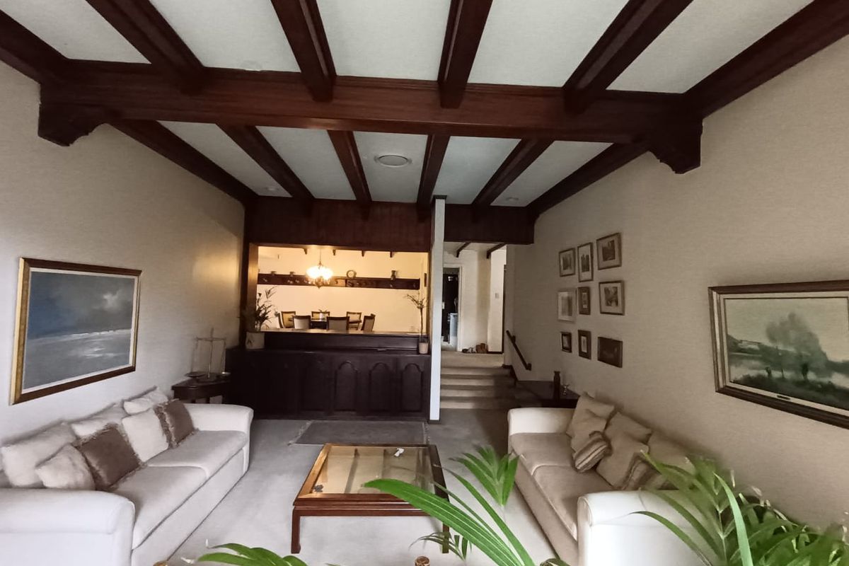 Spacious living room featuring exposed timber ceiling beams, a built-in bar area, and carpeted flooring, leading to an elevated dining space.