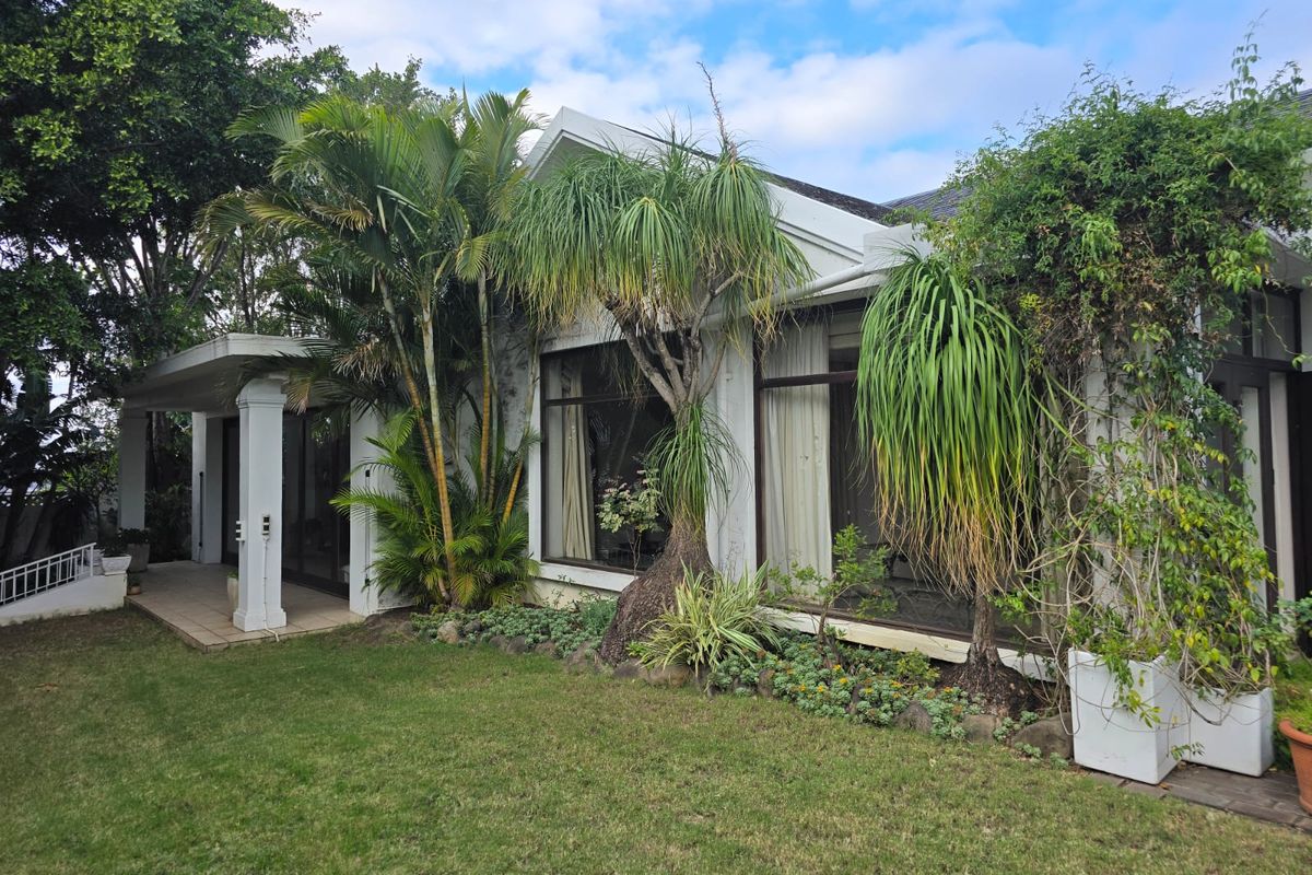 A well-maintained rear exterior view featuring a covered patio, large glass sliding doors, and established garden landscaping.