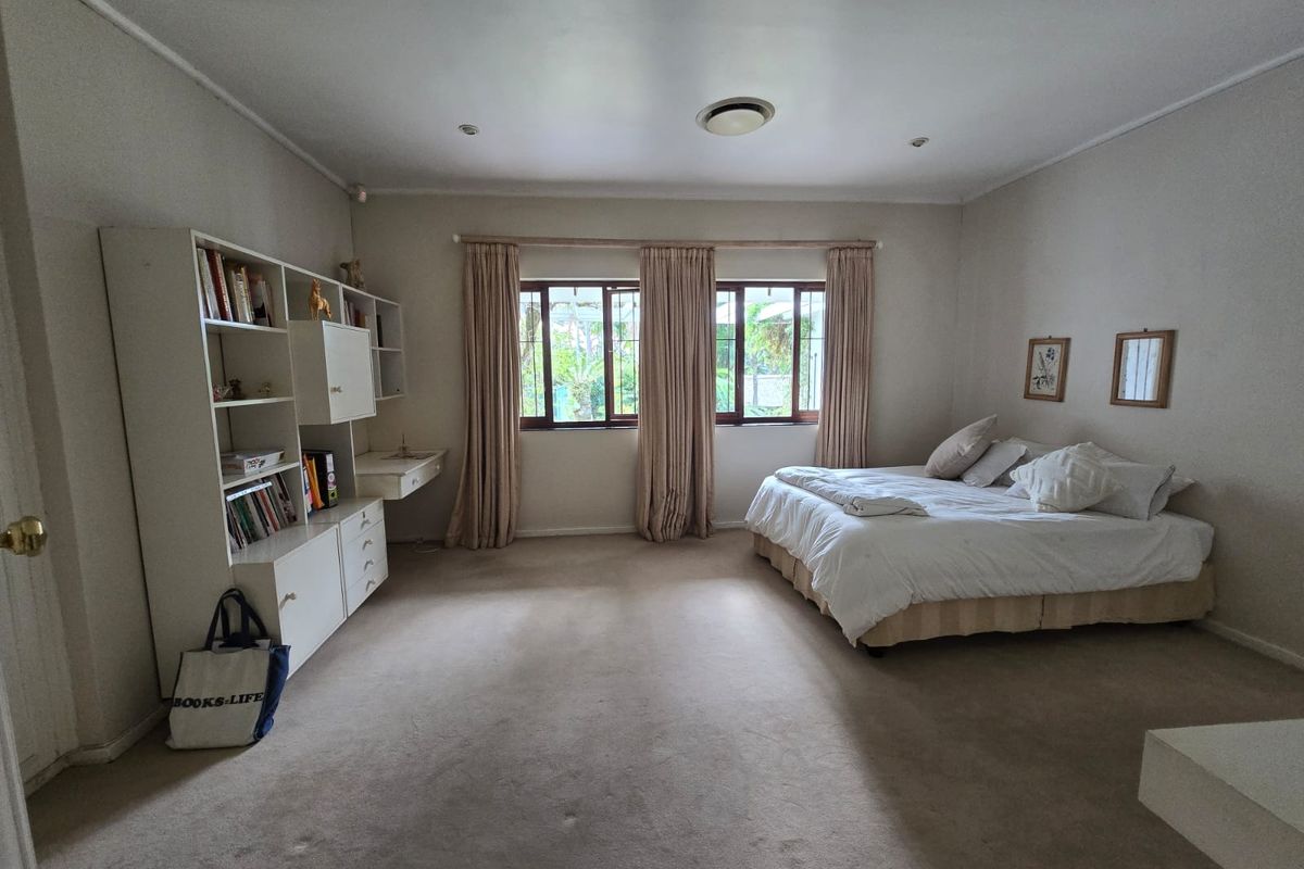 Spacious bedroom featuring neutral walls, carpet flooring, built-in shelving unit, and large windows allowing natural light.