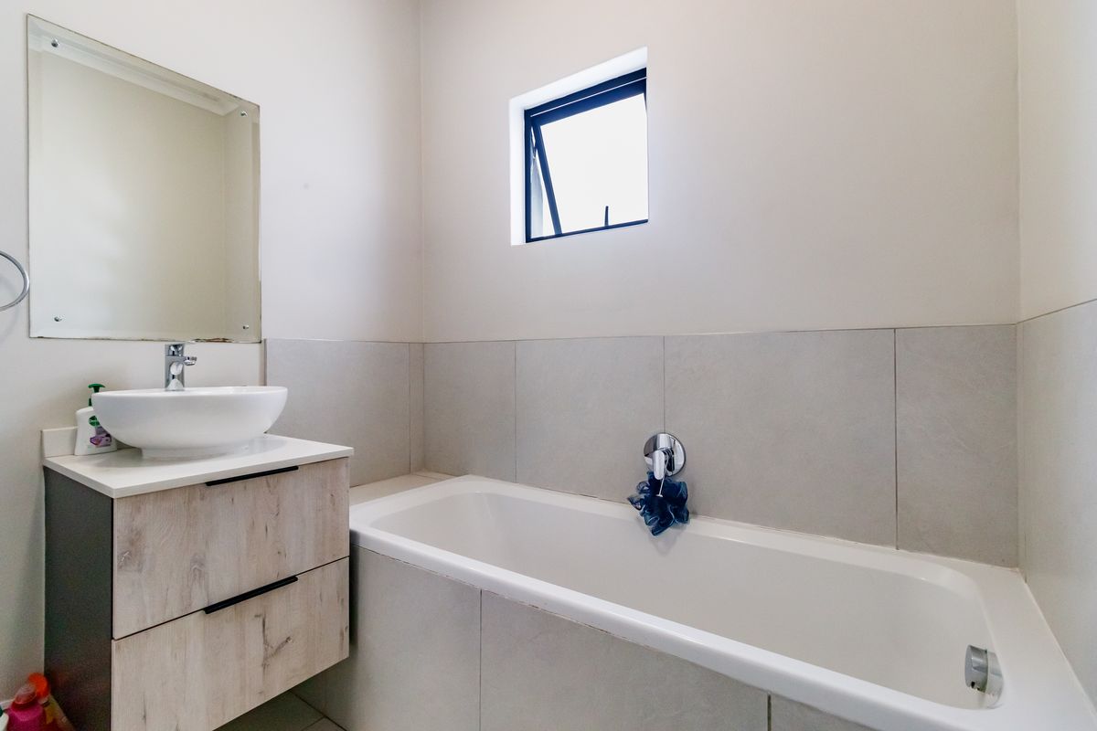 A clean, modern bathroom featuring a floating wood-finish vanity, vessel sink, and a built-in bathtub with neutral wall tiling.