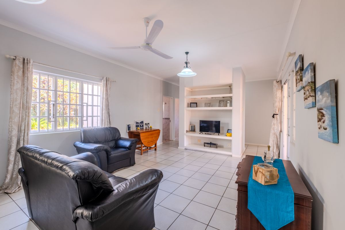 A spacious living room featuring tiled flooring, a ceiling fan, and a built-in shelving unit, offering a functional and well-lit living space.
