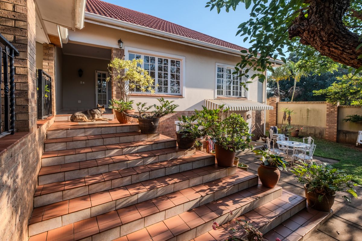 A rear exterior view of the house featuring a wide tiled staircase leading to a covered entrance, brick facade, and a paved patio area.