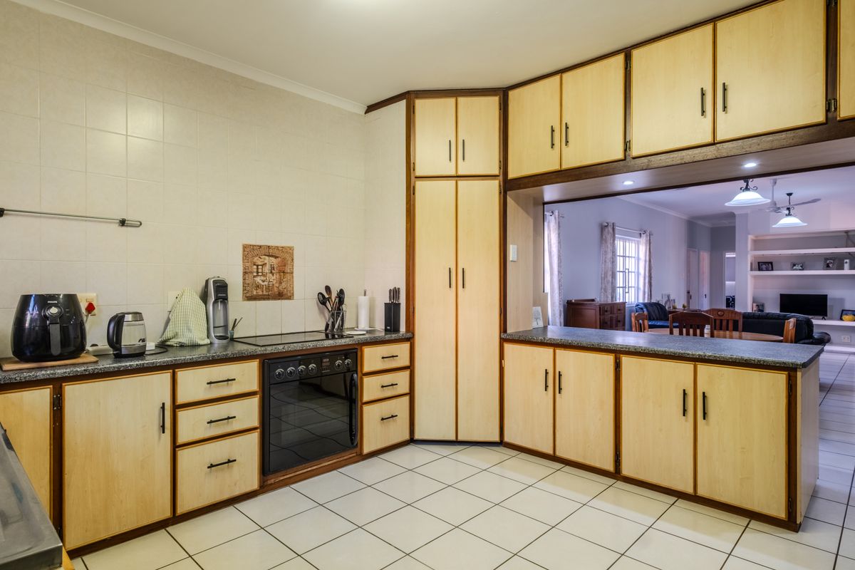A functional kitchen featuring light wood-finish cabinetry, laminate countertops, ceramic tile flooring, and a breakfast bar overlooking the adjacent living area.