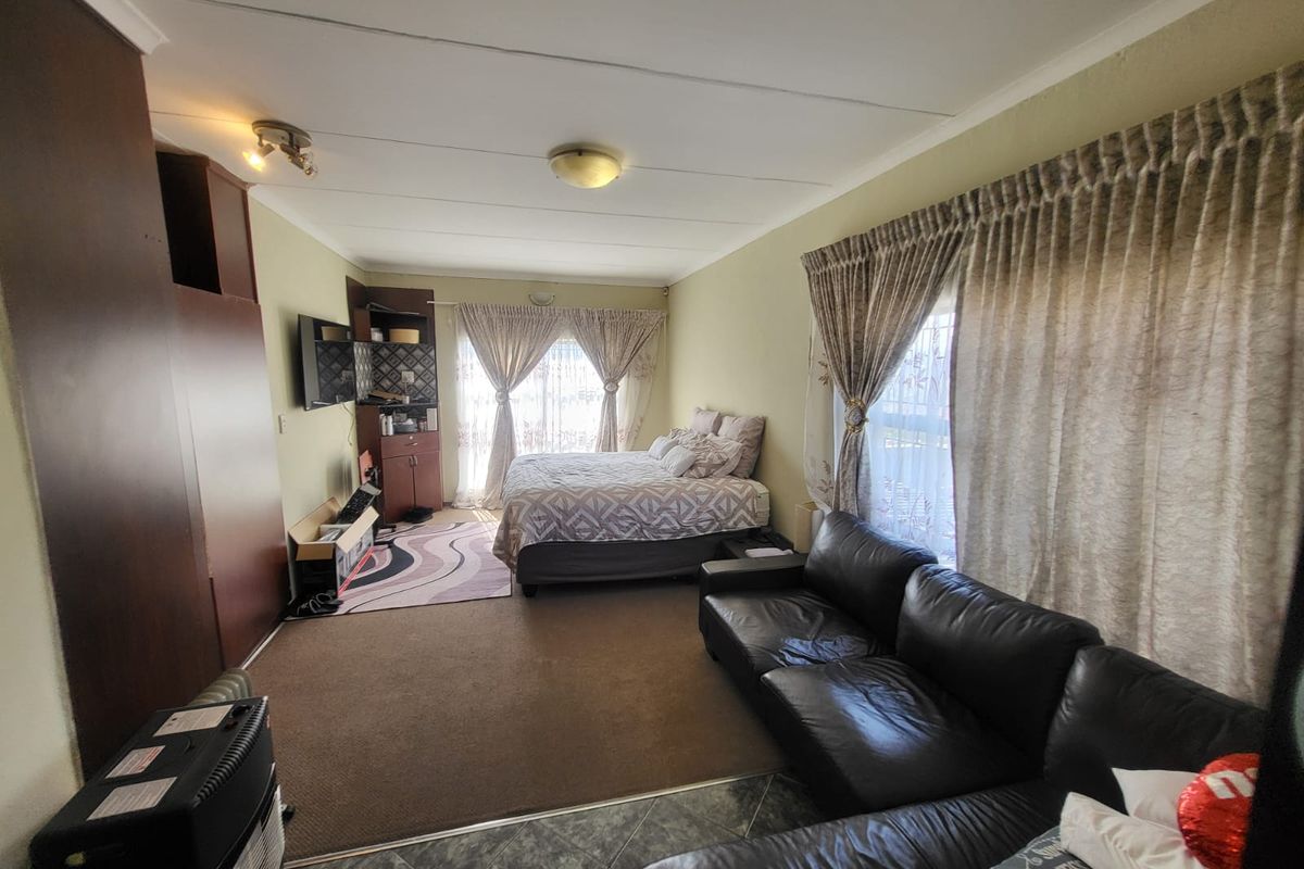 A spacious bedroom featuring built-in cupboards, a combination of tiled and carpeted flooring, and large windows with curtains.