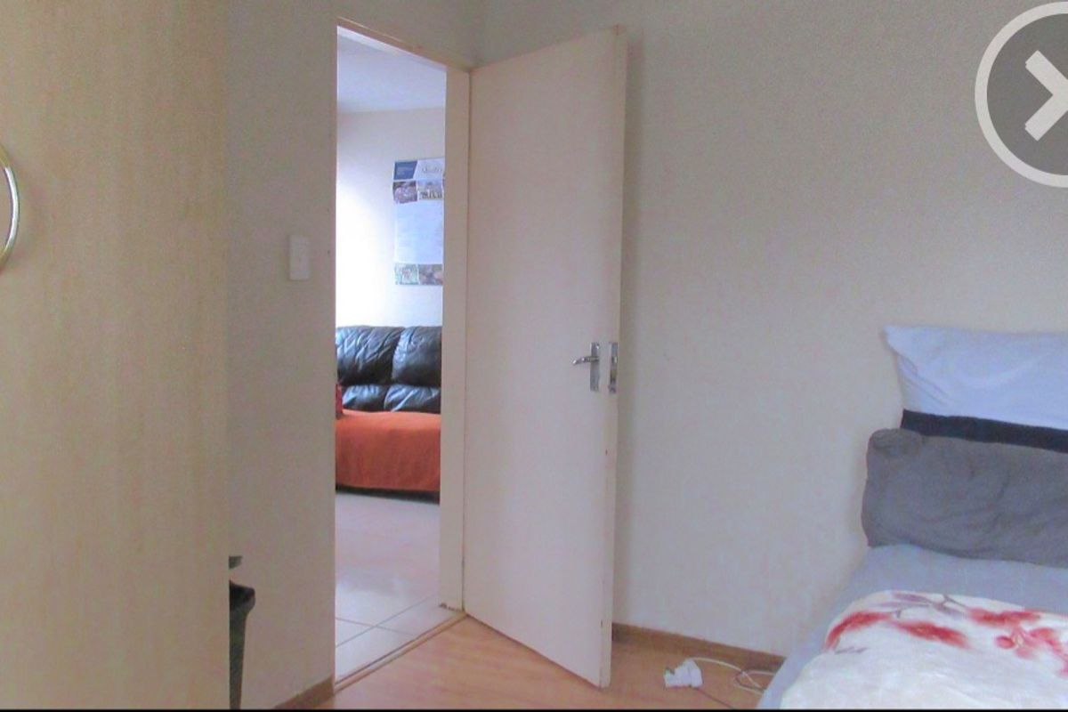 A bedroom featuring laminate flooring and a doorway leading to an adjacent living area.