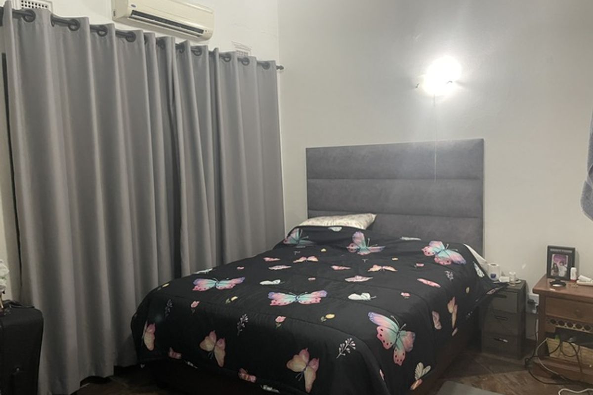 A bedroom featuring a wall-mounted air conditioning unit, a grey upholstered headboard, and a wall sconce light fixture.