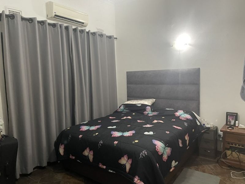A bedroom featuring a wall-mounted air conditioning unit, a grey upholstered headboard, and a wall sconce light fixture.