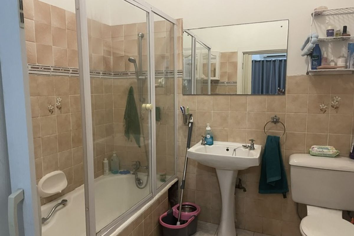 A functional bathroom featuring a pedestal basin, bathtub with glass screen, and wall-mounted mirror, finished with dated ceramic wall tiling.