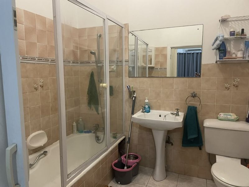 A functional bathroom featuring a pedestal basin, bathtub with glass screen, and wall-mounted mirror, finished with dated ceramic wall tiling.