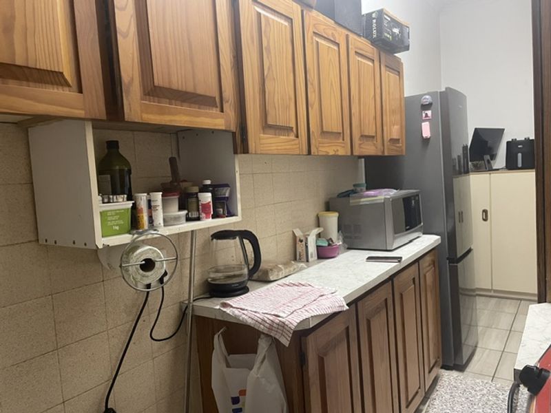 A functional kitchen featuring traditional wooden cabinetry, tiled backsplash, and laminate countertops, offering a dated aesthetic ready for modernization.