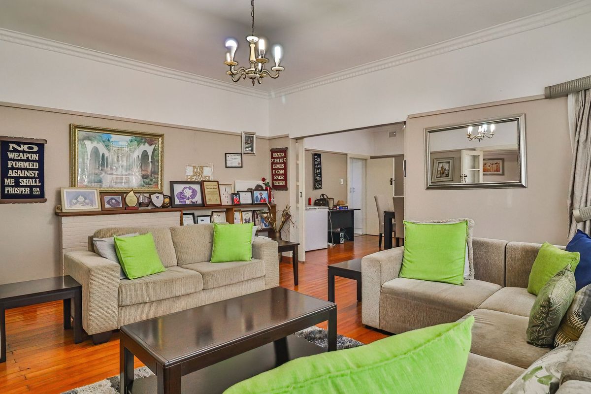Spacious living room featuring warm hardwood flooring, classic crown molding, and a central chandelier, providing a comfortable and inviting atmosphere.