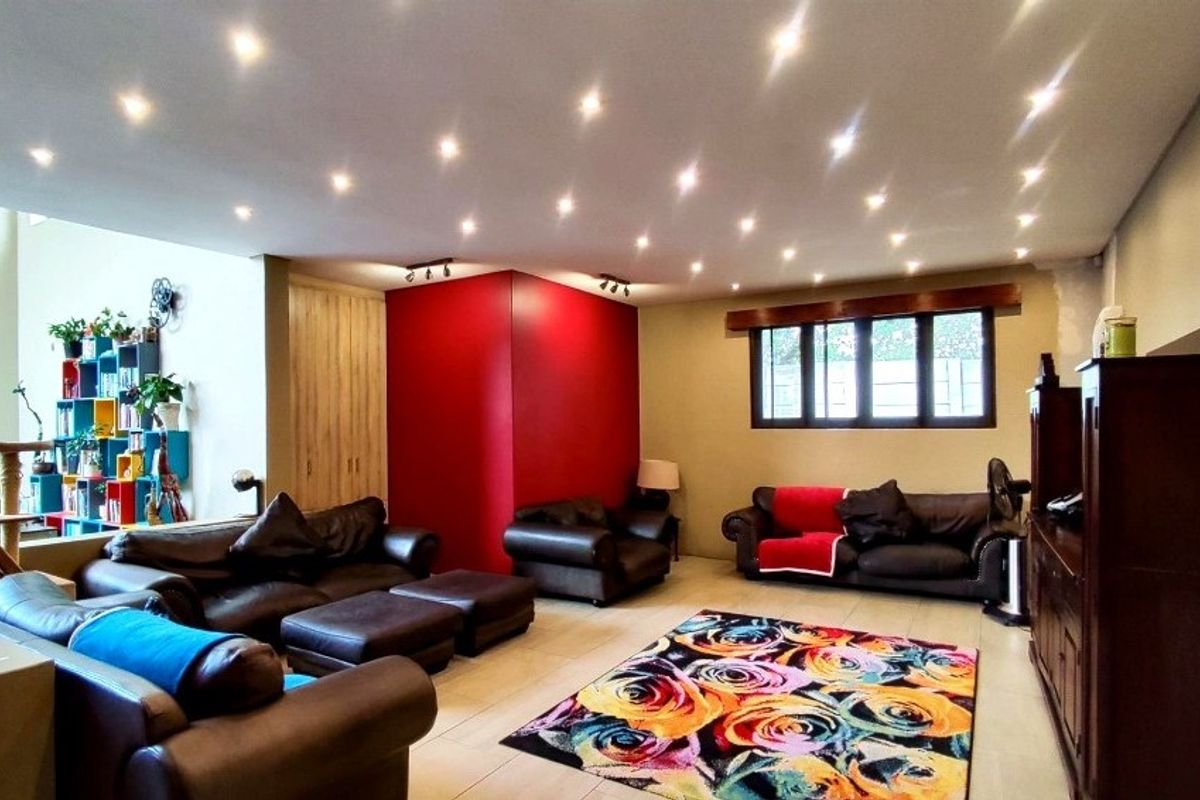 Spacious living room featuring recessed ceiling downlights, tiled flooring, and a bold red accent wall, creating a warm and inviting atmosphere.