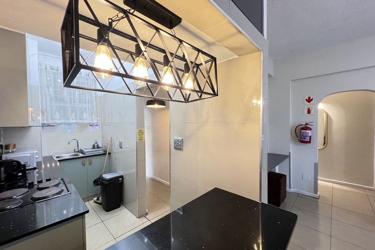 A functional kitchen area featuring dark stone countertops, built-in cabinetry, a modern pendant light fixture, and tiled flooring.