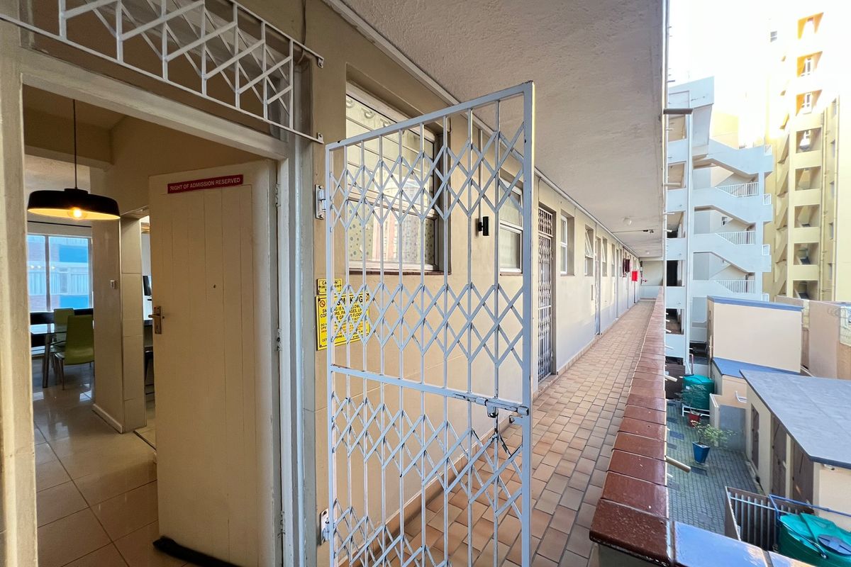 Exterior view of an apartment entrance featuring a security gate, tiled walkway, and access to the building corridor.