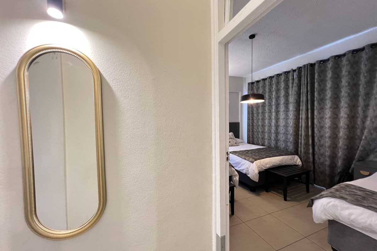 A view from a hallway into a bedroom featuring tiled flooring, a pendant light fixture, and floor-to-ceiling curtains.