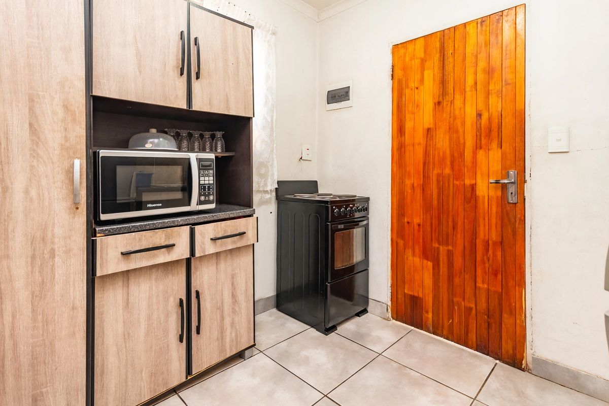 A functional kitchen area featuring wood-look cabinetry, a freestanding stove, tiled flooring, and a solid timber door.