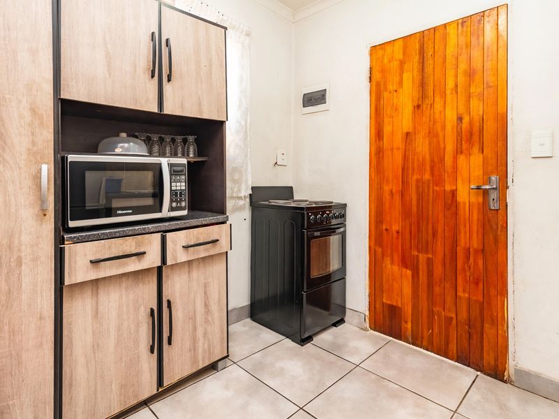 A functional kitchen area featuring wood-look cabinetry, a freestanding stove, tiled flooring, and a solid timber door.