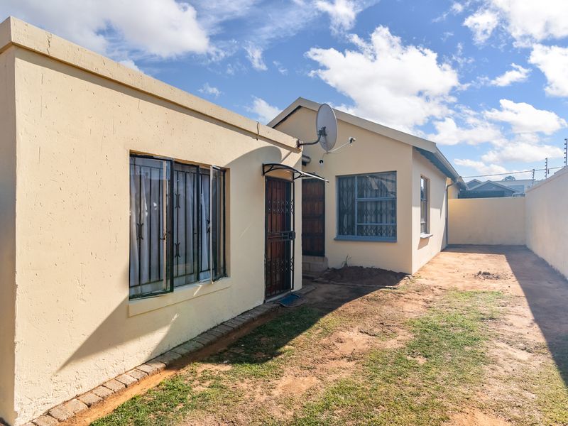 Rear exterior view of the property featuring a paved walkway, security gates, and a boundary wall with a small garden area.