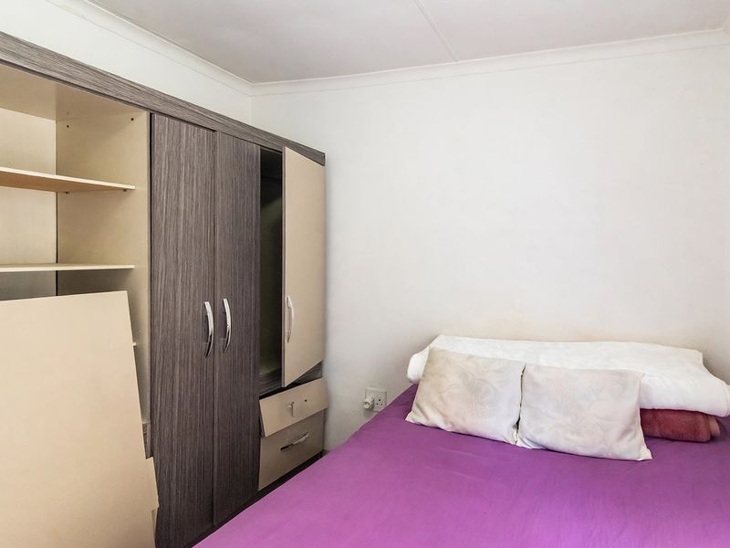 A compact bedroom featuring a built-in wardrobe with some visible wear and damage to the cabinetry.