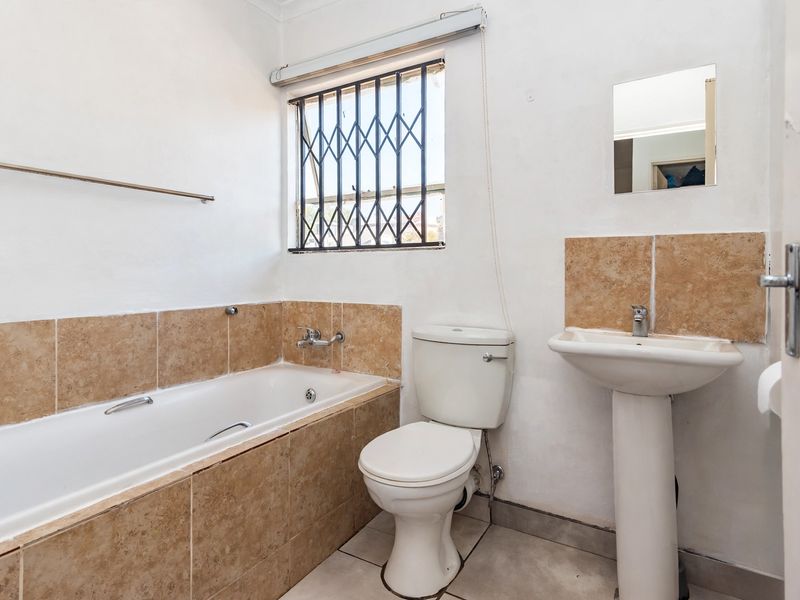 A functional bathroom featuring a bathtub, pedestal basin, and toilet, with tiled splashbacks and a security gate on the window.