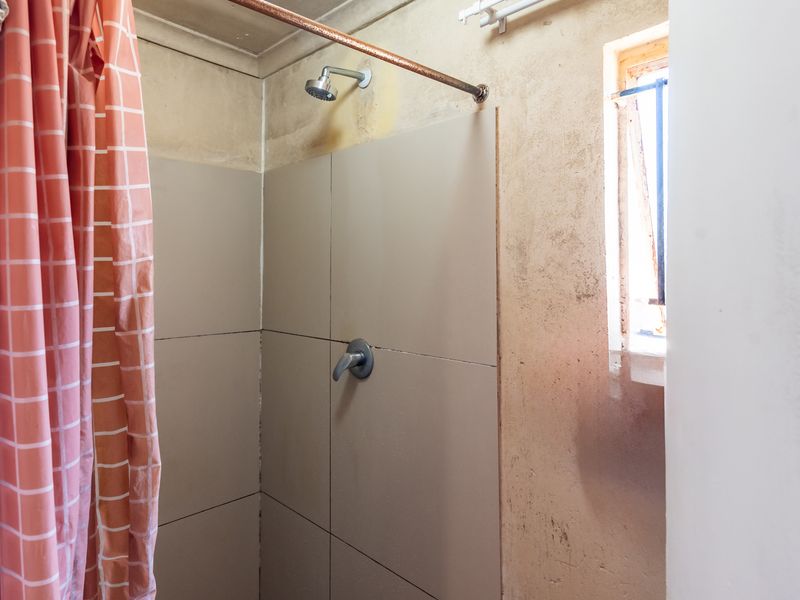 A basic shower area featuring tiled walls and a window with security bars, currently showing significant wear and requiring cosmetic updates.