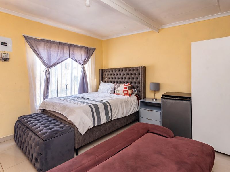 A bedroom featuring tiled flooring and an exposed ceiling beam, with visible wall imperfections and exposed electrical conduit.