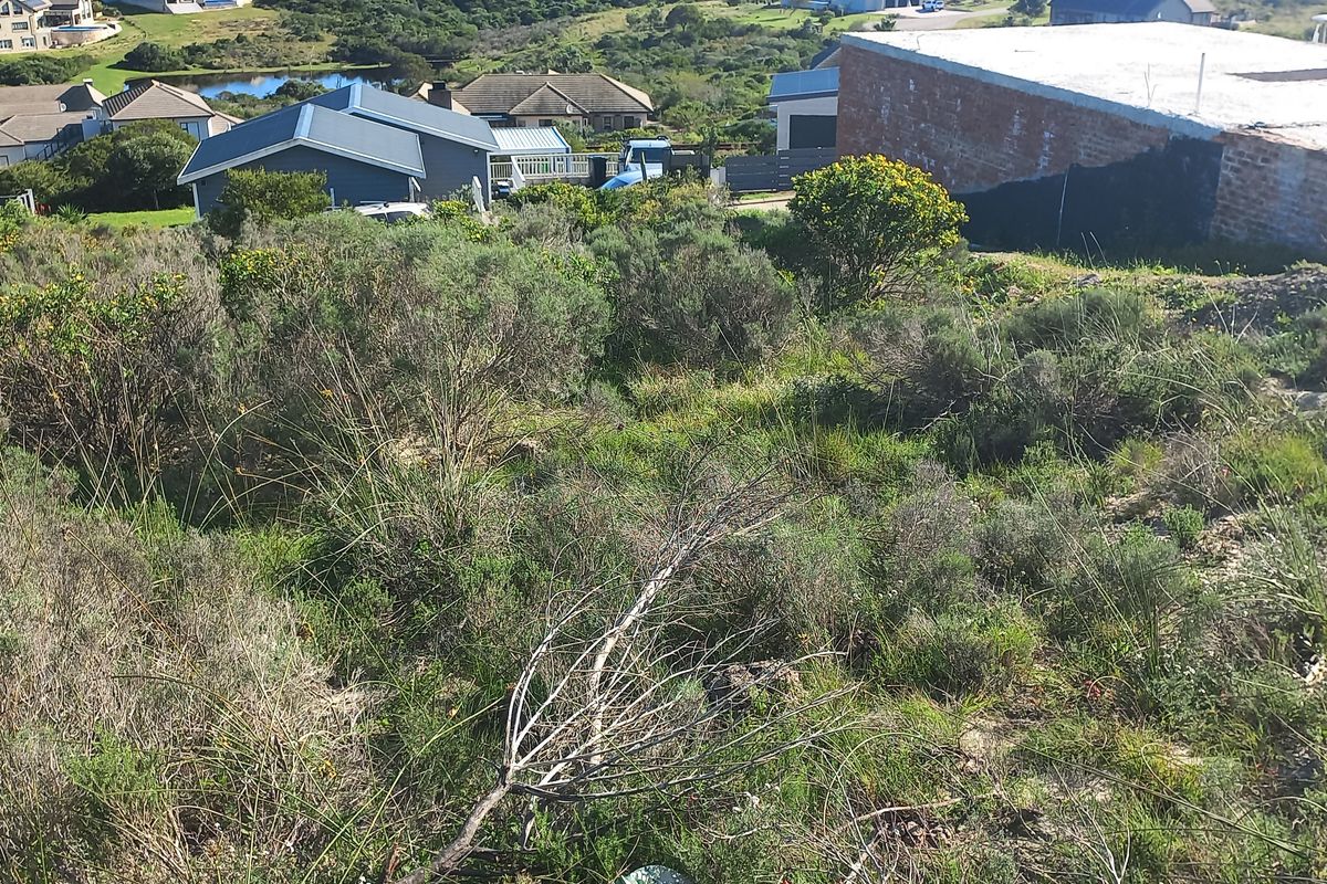 An elevated view of a sloped residential vacant land plot featuring natural vegetation and surrounding neighborhood development.