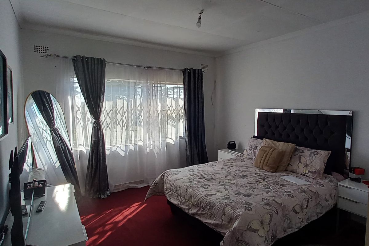 A bedroom featuring a large window with security gate, carpeted flooring, and basic ceiling lighting.