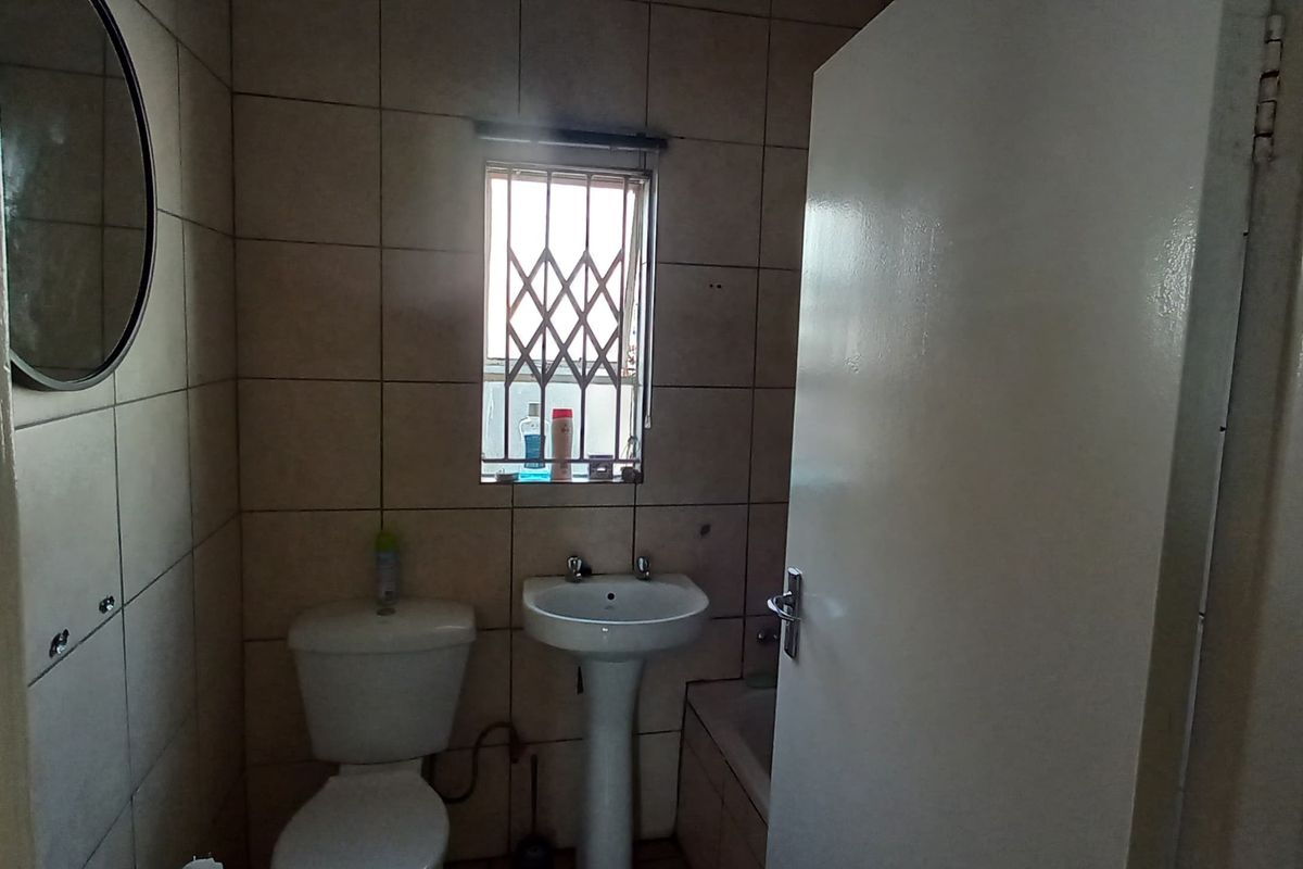 A functional bathroom featuring a pedestal basin, toilet, and tiled walls with a security-grille window.