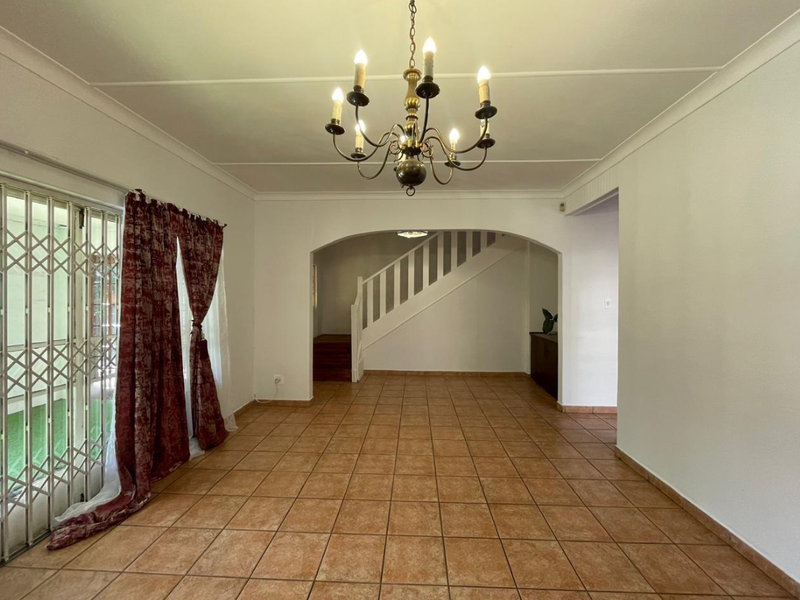 An open-plan living area featuring ceramic tile flooring, a decorative archway leading to a staircase, and a classic chandelier.
