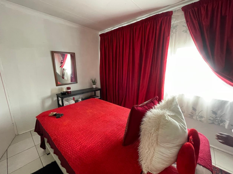 A bedroom featuring tiled flooring and large window curtains, providing a functional space with neutral wall finishes.