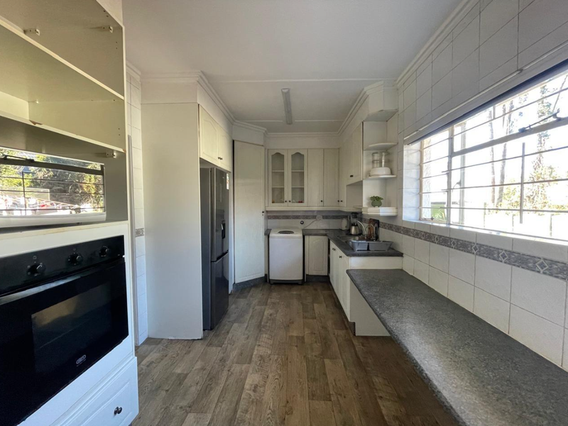 A functional kitchen featuring laminate countertops, tiled splashbacks, built-in oven, and wood-look flooring, offering a practical layout with ample storage space.
