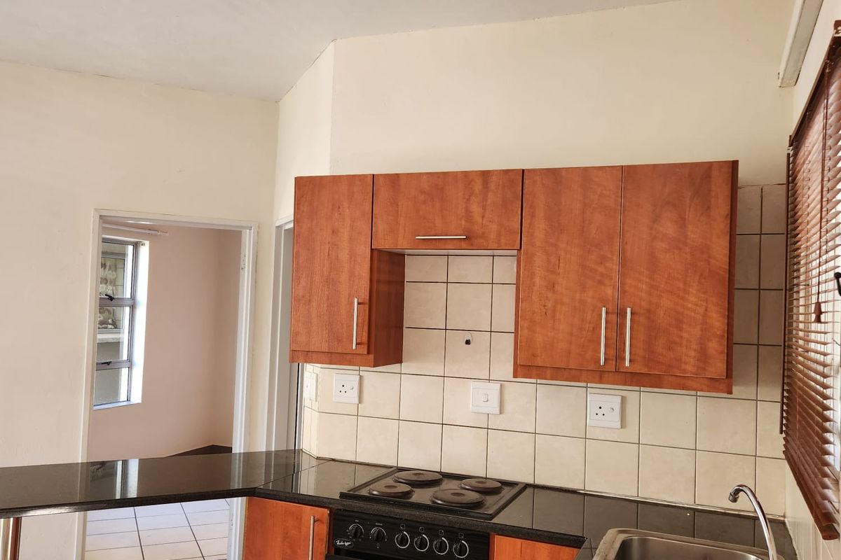 A functional kitchen featuring dark granite countertops, wooden cabinetry, a built-in oven with hob, and tiled splashbacks, with an adjacent tiled living area.