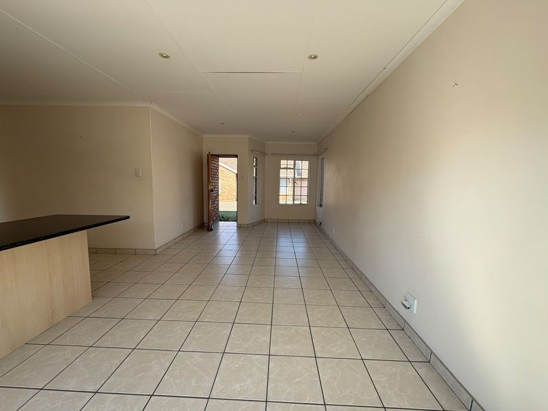 Spacious open-plan living area featuring neutral tiled flooring, recessed lighting, and a breakfast bar, offering a blank canvas for interior design.