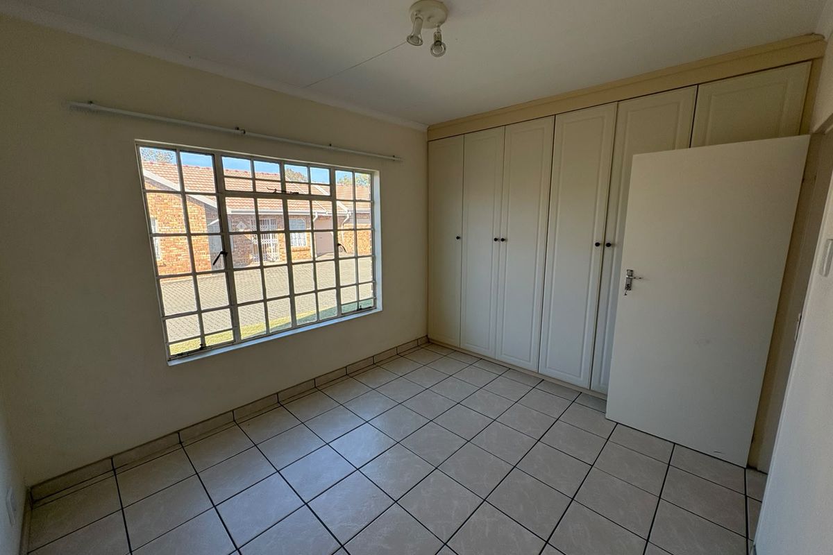 A bright, empty bedroom featuring neutral tiled flooring and extensive built-in cupboard storage, offering a clean canvas for personalization.