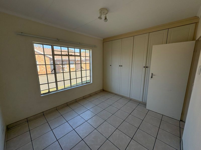 A bright, empty bedroom featuring neutral tiled flooring and extensive built-in cupboard storage, offering a clean canvas for personalization.