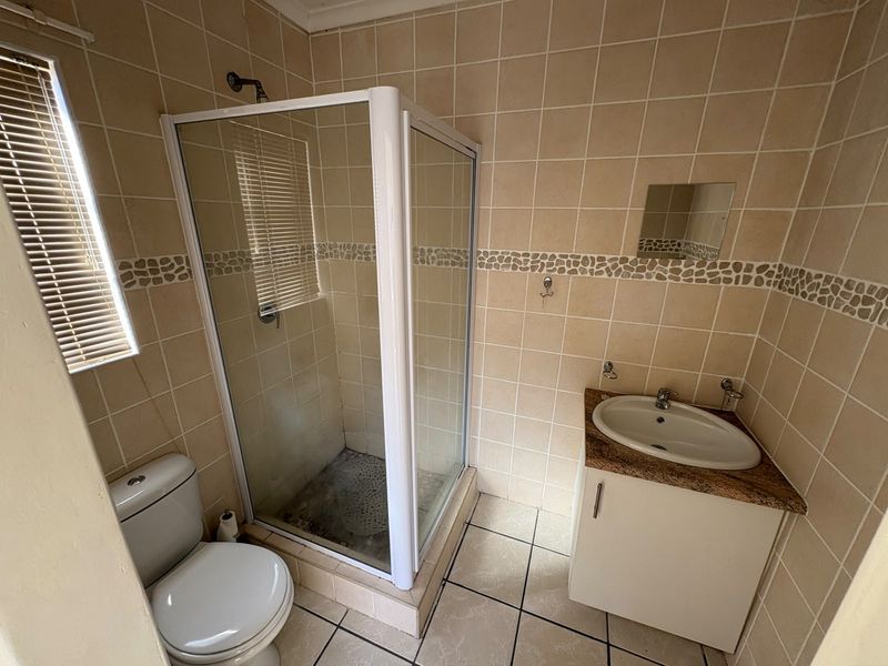 A functional bathroom featuring a corner shower enclosure, vanity cabinet with basin, and tiled finishes throughout.