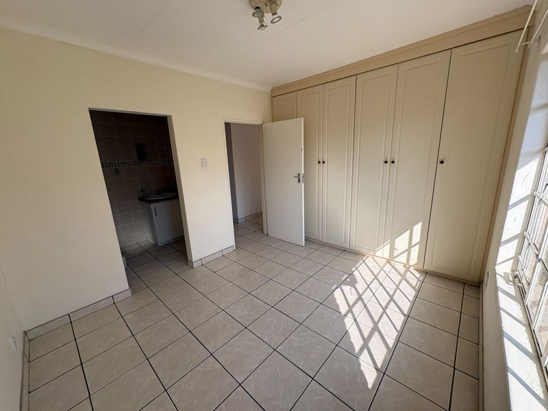 A bright, empty bedroom featuring neutral tiled flooring, extensive built-in cupboards, and an adjoining small utility or wash area.