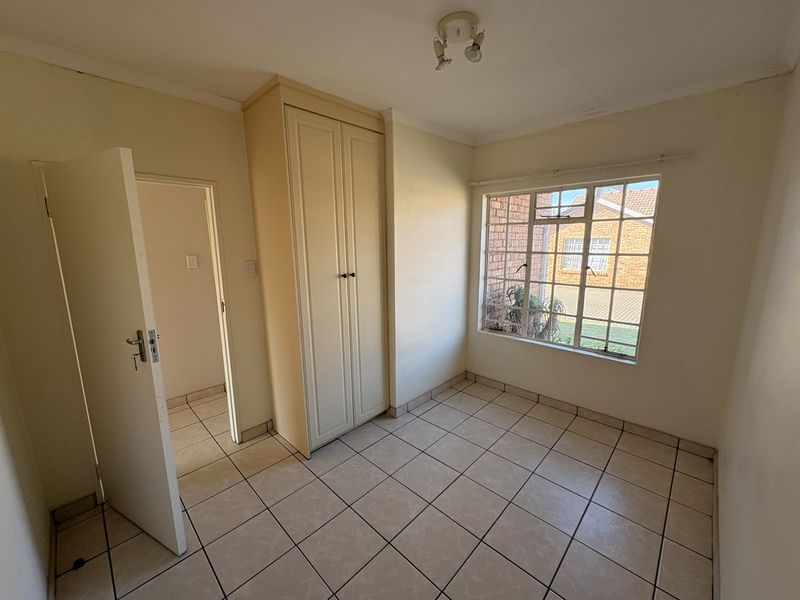 A bright, empty bedroom featuring tiled flooring, a built-in wardrobe, and a window with security bars, offering a clean canvas for personalization.