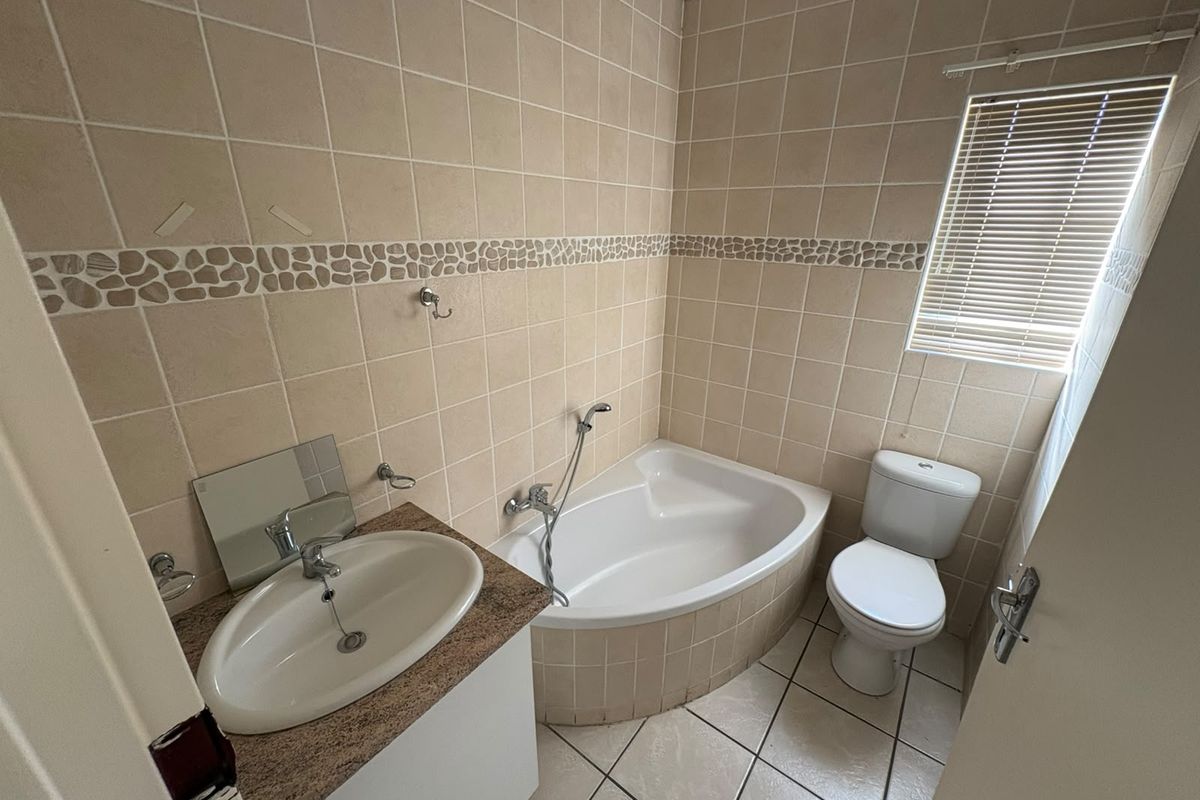 A functional bathroom featuring a corner bathtub, vanity basin, and toilet, finished with neutral wall and floor tiling.