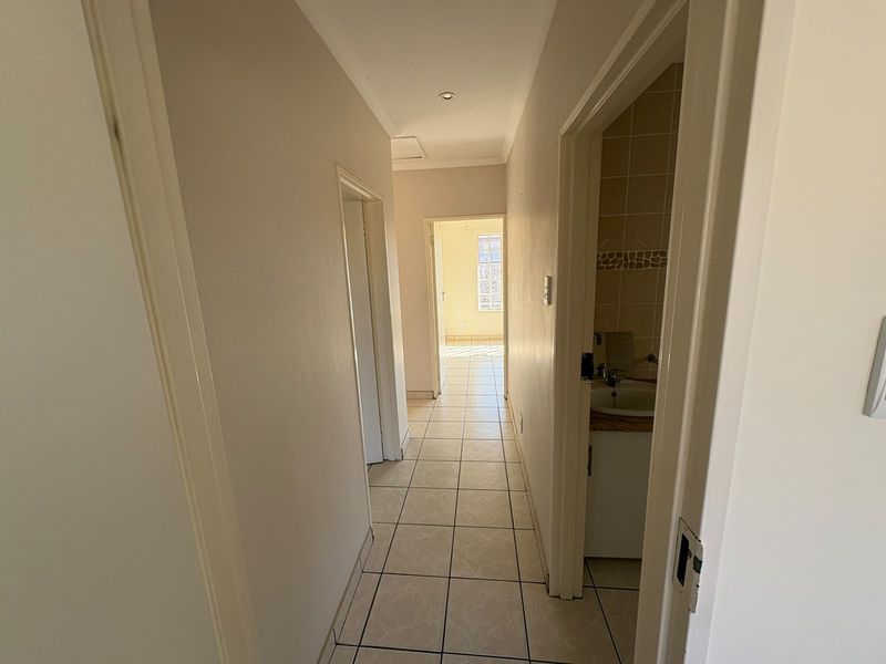 A neutral hallway with tiled flooring leading to adjacent rooms, featuring a glimpse of a bathroom vanity area.