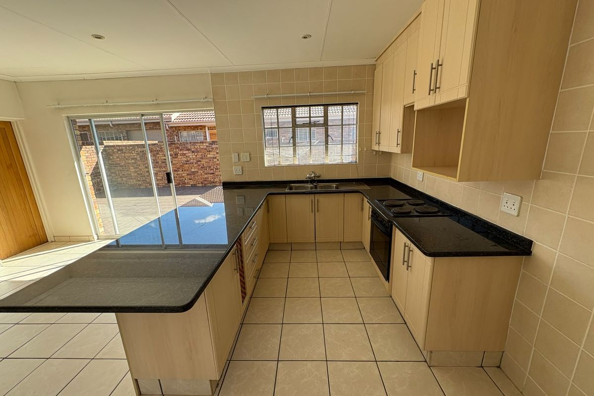 A functional kitchen featuring light wood cabinetry, dark granite countertops, built-in oven, and tiled finishes, with direct access to an outdoor patio area.