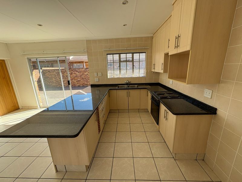 A functional kitchen featuring light wood cabinetry, dark granite countertops, built-in oven, and tiled finishes, with direct access to an outdoor patio area.