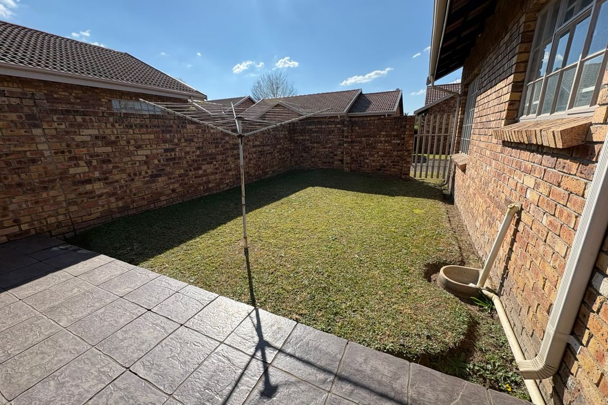 A private rear garden featuring a paved patio area, a small lawn, and brick boundary walls, providing a low-maintenance outdoor space.