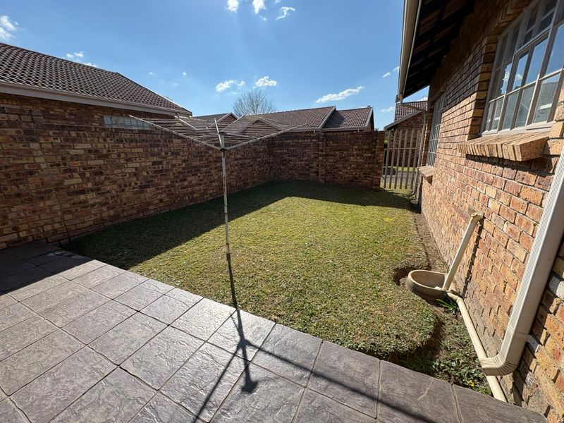 A private rear garden featuring a paved patio area, a small lawn, and brick boundary walls, providing a low-maintenance outdoor space.